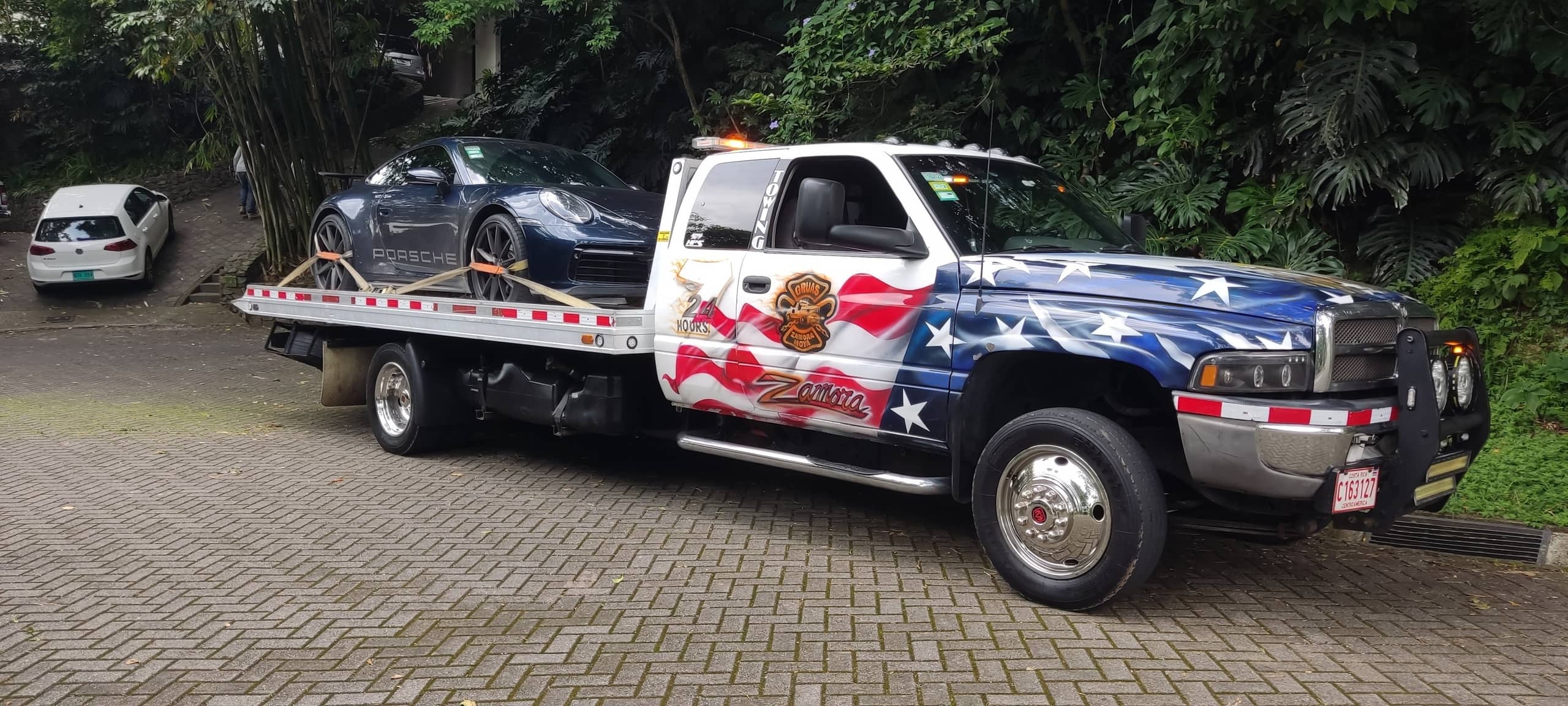 Grúa de plataforma de Grúas Zamora Moya con la bandera de Estados Unidos pintada, cargando un vehículo en Costa Rica